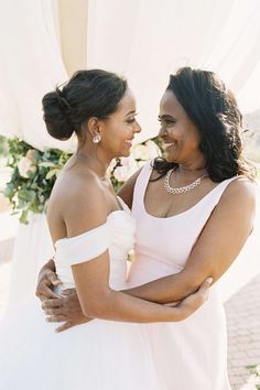 two women in white dresses standing next to each other under a canopy with flowers on it