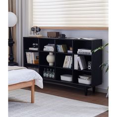 a black book shelf with books on it in a living room next to a window