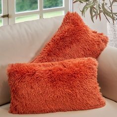 two orange pillows sitting on top of a white couch next to a potted plant