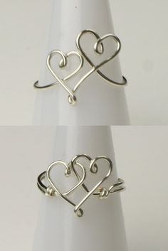 two silver rings with hearts on them sitting on top of a white table next to each other