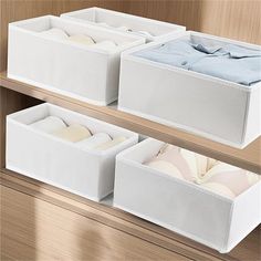 three white bins with clothes in them sitting on top of a wooden shelf next to each other