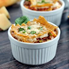 two white bowls filled with lasagna casserole on top of a wooden table