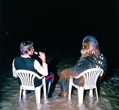 two people sitting on chairs in the water, one is dressed as darth vader