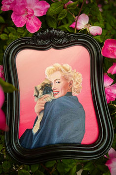 a painting of a woman holding a small dog in front of pink and green flowers