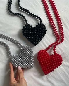 three beaded heart pendants are shown on a white sheet, one is red and the other is black