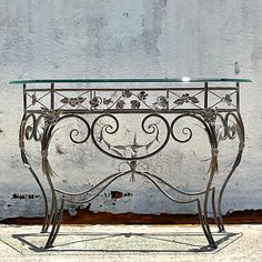 an iron and glass console table against a white stucco wall with flowers on the top