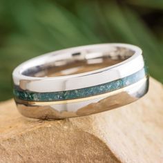 a wedding band with green and blue stone inlays sits on top of a rock