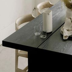 a black table with two vases on it and some chairs in front of it