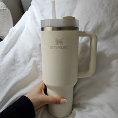 a person is holding a travel mug in their hand on a bed with white sheets