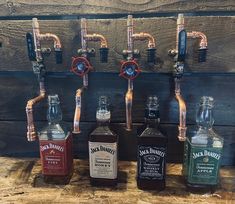 four bottles of liquor lined up in front of a wall mounted faucet with pipes