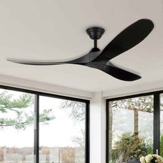 a black ceiling fan in a white living room with large windows and sliding glass doors