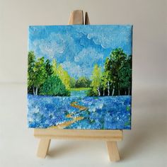 an easel with a painting on it that has blue grass and trees in the background