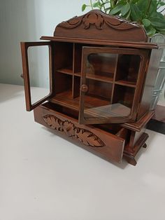 an old wooden cabinet with glass doors on the top and bottom shelf is sitting on a table next to a potted plant