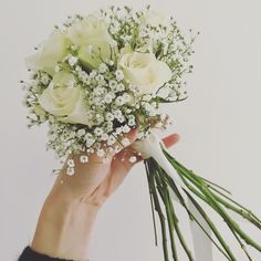 a hand holding a bouquet of white roses and baby's breath flowers in it