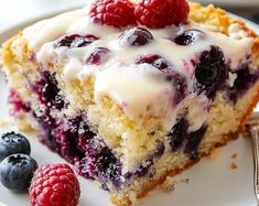 a close up of a slice of cake on a plate with raspberries and blueberries