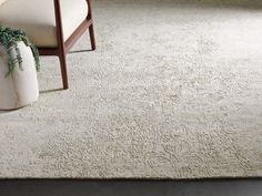 a white rug with a chair and potted plant on the floor next to it