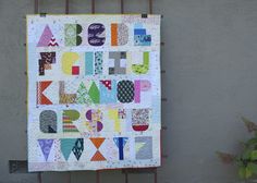 a quilt hanging on the side of a building that says abc, k, and q