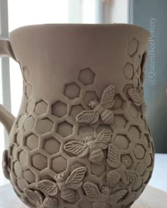 a ceramic vase with bees and honeycombs on the outside, sitting on a table