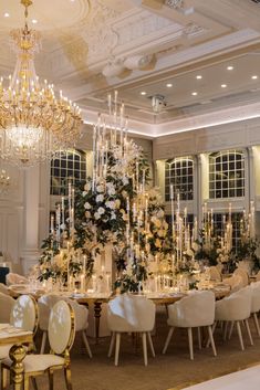 a room filled with lots of tables covered in white flowers and chandelier hanging from the ceiling