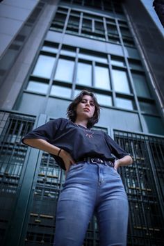 a woman standing in front of a tall building with her hands on her hips and looking off to the side