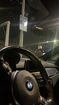 the interior of a bmw car with its steering wheel and dashboard lights on at night