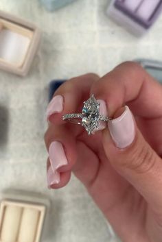 a woman's hand holding an engagement ring in front of some other jewelry items