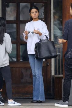 a woman in white sweater and jeans holding a black bag while standing next to other people