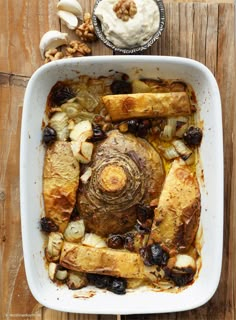 a casserole dish with bread, onions and olives in it on a wooden table