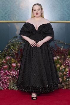 a woman in a black dress standing on a red carpet with pink flowers behind her