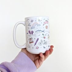 a person holding up a coffee mug with various things on it and in the background is a white wall