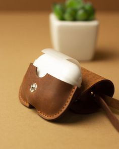 a brown leather case with a white cup in it sitting on a table next to a potted plant