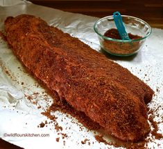 a large piece of meat sitting on top of wax paper next to a bowl of seasoning