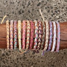 several different colored braided bracelets on top of a wooden stick in front of a stone wall