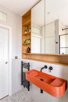 an orange sink in a bathroom next to a mirror and shelf with plants on it