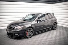 a black car parked in a garage with checkered flooring and white walls behind it