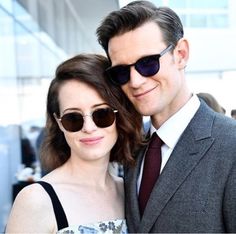 a man in a suit and sunglasses standing next to a woman