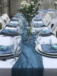 a table set with blue and white place settings, flowers in vases, and napkins