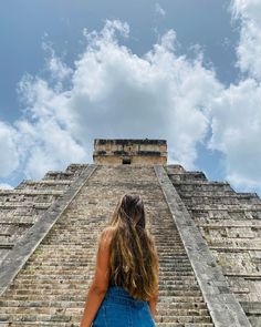 a woman standing in front of an ancient pyramid with her back to the camera looking up