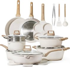 an assortment of white pots and pans with wooden spoons, spatulas and utensils