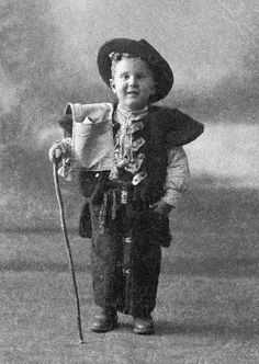 black and white photograph of a young boy wearing a hat, vest and holding a cane