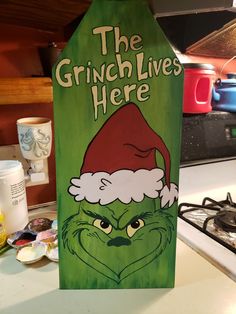 the grinch lives here sign with santa's hat on it sitting on a kitchen counter