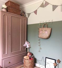 a room with pink and green walls, wicker baskets on the floor and a wooden cabinet