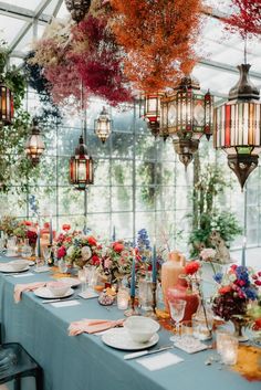 a long table is set with plates and place settings for an elegant dinner party in a greenhouse