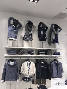 clothing on display in a store with white shelving and shelves filled with blue shirts