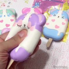 someone is holding two unicorn popsicles in their hand, one has a toothpick on it