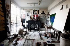 an art studio with various pieces of artwork on the floor and walls covered in clutter