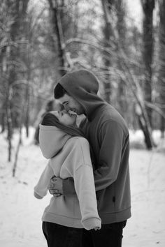 black and white photograph of a couple kissing in the snow with trees in the background