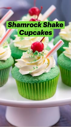 cupcakes with white frosting and green icing topped with cherries on a plate