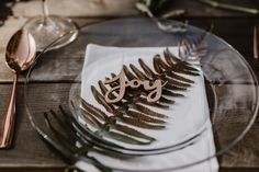 a glass plate topped with a wooden cut out of the word joy next to a fork and knife