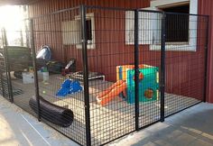 an outdoor play area in front of a red building with black metal fence and door